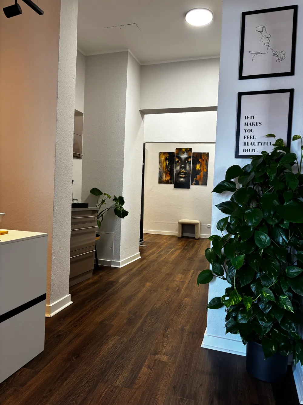 Blick vom Empfang in den Flur der Praxis mit Bildern an der Wand und Zimmerpflanze