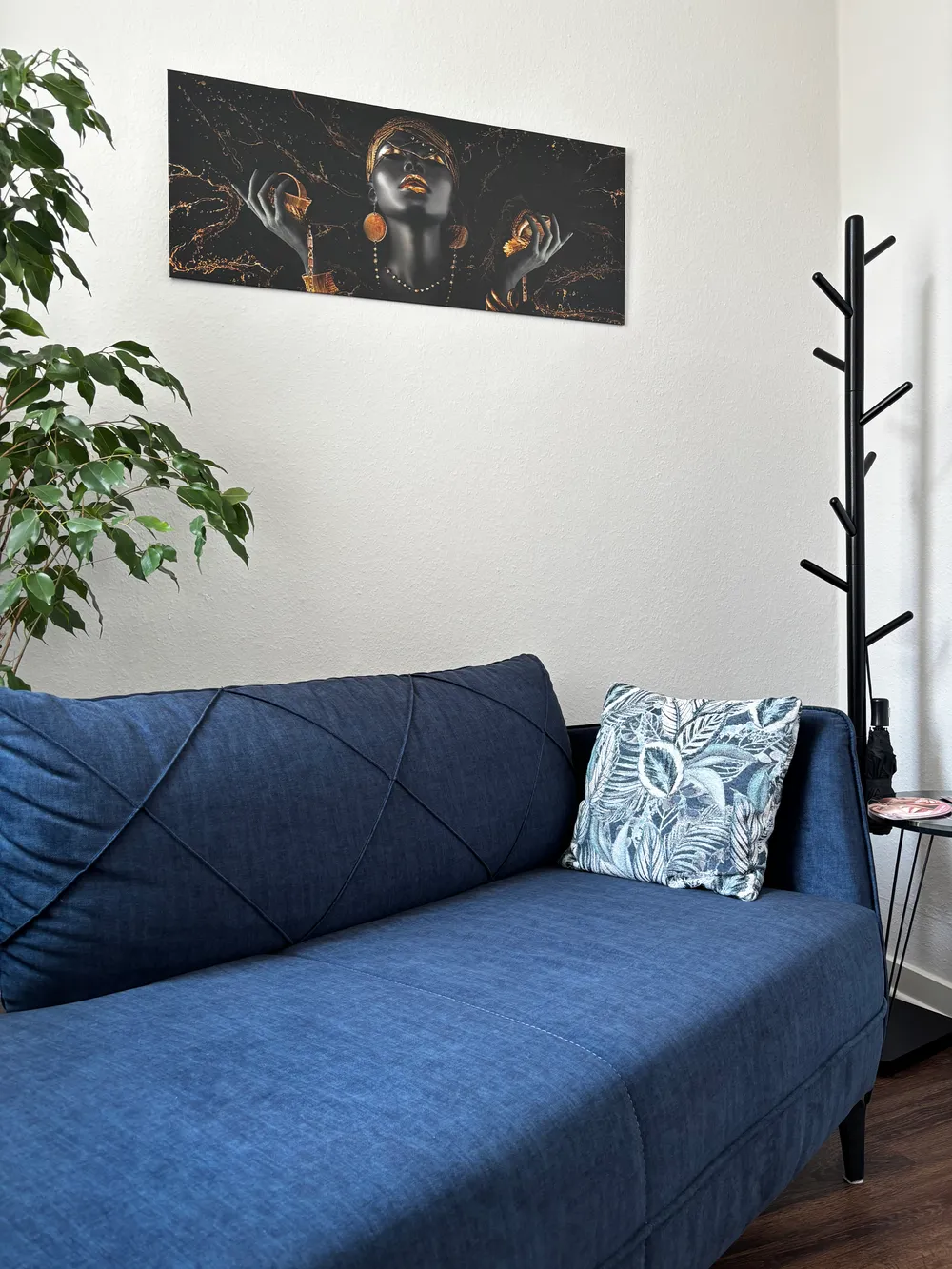 Wartebereich der Praxis mit blauem Sofa, Zimmerpflanze und Wandbild